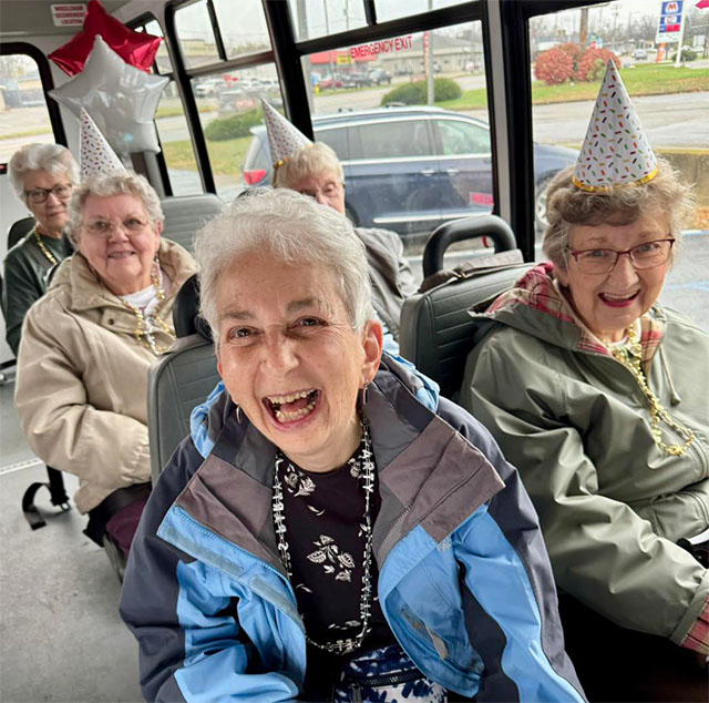 Party-ladies-cropped Group of senior ladies wearing party hats, smiling and sitting together on the Lakeview bus during a community outing.